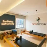 Fizyofactory pilates stüdyosunda reformer ekipmanları ve motivasyon yazısı bulunan modern egzersiz alanı.